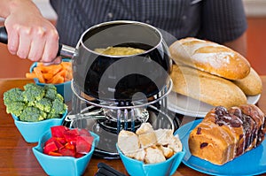 Close up of cheff preparing a gourmet Swiss fondue dinner with assorted cheeses and a heated pot of cheese fondue and