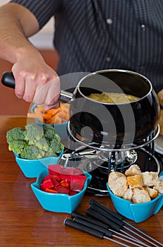 Close up of cheff preparing a gourmet Swiss fondue dinner with assorted cheeses and a heated pot of cheese fondue and