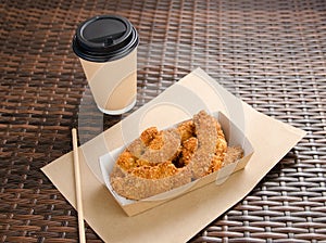 Close-up of chicken in batter in disposable case next to coffee in a paper cup. Unhealthy fast food