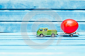 Close up of chicken egg on toy car with a trailer on a blue wooden background