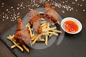 Close-up of chicken legs and fries on a slate plate