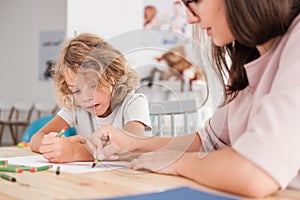 Child with an autism spectrum disorder and the therapist by a table drawing with crayons during a sensory