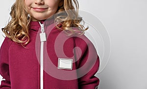 Close-up of a child in a burgundy jumpsuit or sweatshirt with a zipper, and a place for a label on a light background