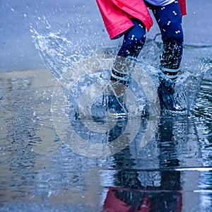 Close up child girl with rain boots jumping in puddles after rain. Childhood, laisure, happiness concept