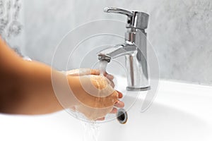 Close-up of child girl, washing her hands under water tap in white sink. Personal hygiene concept.