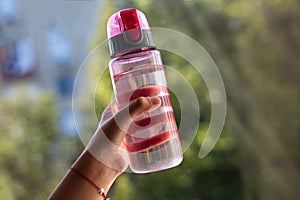 Close-up of child hand holding pink bottle for water.