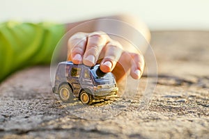 Close-up of a child hand is playing with a blue toy-car outdoor. A child is playing with a toy car