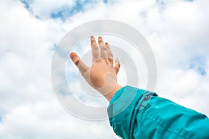 Close up of child hand raised up over blue sky and clouds background. Gesture