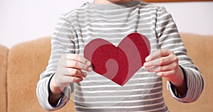 Close-up of child hands holding a red heart-shaped postcard and showing her to the camera. Valentine's day concept.