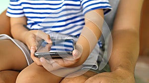 Close up of child hands holding and using smartphone outdoor in hug of father at home.