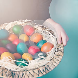 Close up of child hands holding a wicker basket full of colorful Easter eggs.