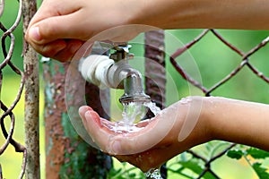 Close up child hands with water drops from old grunge brass faucet on green bokeh background. Water shortage and earth day