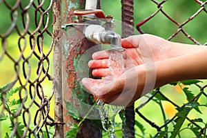 Close up child hands with water drops from old grunge brass faucet on green bokeh background. Water shortage and earth day