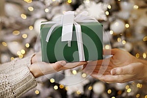 Close up of child and mother hands with gift box over christmas tree lights background. Christmas holidays, present, happiness