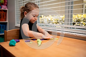 Close up of child playing with play dough in a playroom on a wood table.