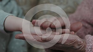 Close-up, a child puts his palm on the wrinkled hand of an elderly person. Grandmother lovingly touches and strokes