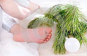 Close up child`s bare feet, child laying on plaid next  branches of Christmas tree, lazy winter holidays concept