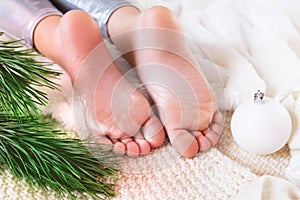 Close up child`s bare feet, child laying on plaid next Christmas tree, lazy winter holidays concept