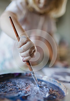 Close-up of child& x27;s hand holding paintbrush, painting with tempera paint.