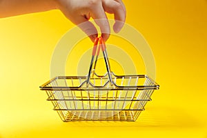 Close up of child`s hand holds handles metal grocery basket for shopping in supermarket with orange plastic elements photo