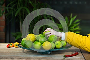 Child's hand reaching to grab a fresh lime from the fruit bowl