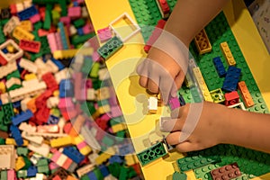 Close up of child`s hands playing with colorful plastic bricks at the table. Early learning. stripe background. Developing toys