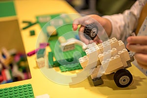 Close up of child`s hands playing with colorful plastic bricks at the table. Early learning. stripe background. Developing toys