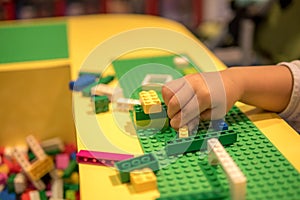 Close up of child`s hands playing with colorful plastic bricks at the table. Early learning. stripe background. Developing toys