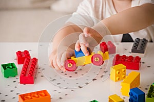 Close up of child`s hands playing with colorful plastic bricks at the table. Toddler having fun