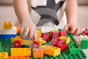 Close up of child`s hands playing with colorful plastic bricks at the table. Toddler having fun