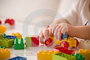 Close up of child`s hands playing with colorful plastic bricks at the table. Toddler having fun and building