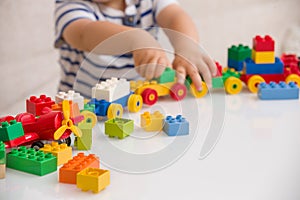 Close up of child`s hands playing with colorful plastic bricks at the table. Toddler having fun and building