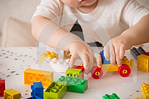 Close up of child`s hands playing with colorful plastic bricks at the table. Toddler having fun and building out of bright