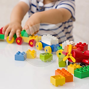 Close up of child`s hands playing with colorful plastic bricks at the table. Toddler having fun and building out of bright