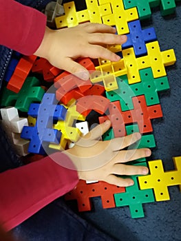 Close up of child`s hands playing with colorful plastic bricks at the table.