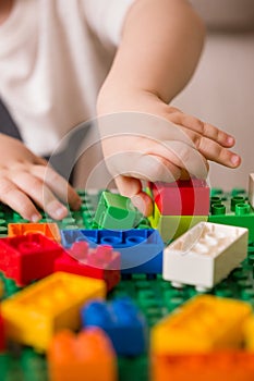 Close up of child`s hands playing with colorful plastic bricks at the table. Toddler having fun. Developing toys