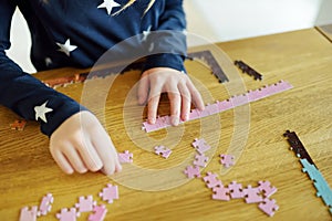 Close-up on child`s hands playing puzzles at home. Child connecting jigsaw puzzle pieces in a living room table. Kid assembling a