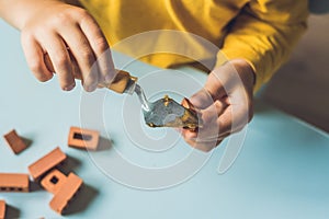 Close up of child`s hands playing with real small clay bricks at the table. Toddler having fun and building out of real small cla