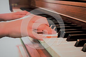 Close up of a child`s hands playing a rustic brown upright piano keyboard