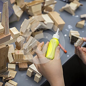 Close-up of child`s hands playing with wooden constructor, bricks on table. Boy glues blocks to make house, building