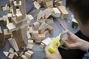 Close-up of child`s hands playing with wooden constructor, bricks on table. Boy glues blocks to make house, building