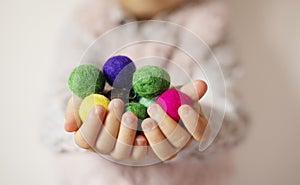 Close up of children hands holding colorful felt balls. Child, kid palms. A little girl keep in handfuls of colored wool balls