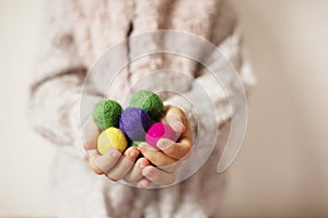 Close up of children hands holding colorful felt balls. Child, kid palms. A little girl keep in handfuls of colored wool balls