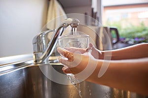 Close up of children hands, pouring glass of fresh water from tap in kitchen