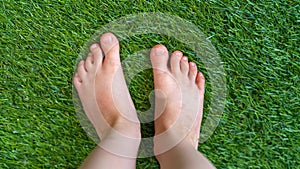 Close-up of children`s feet standing barefoot on a green surface, grass