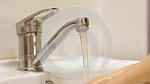 Close-up of children`s hands are washed under water in the sink in the bathroom. Hand washing baby hygiene.Water flows from the ba