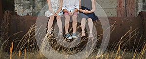 Close up of children`s legs, three siblings sitting on a rusty pipe