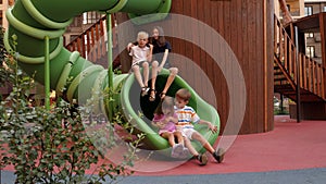 Close-up of children sitting on a plastic slide on the playground and laughing.