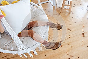 Close-up of a childs brown Brogue shoes sitting on macrame chair swing. Rustic style in the interior