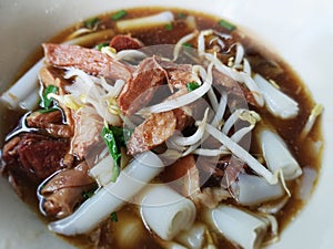 Close up chinese roll noodle soup In a white bowl. Popularly put the pork in boiled water in the sauce and vegetables.